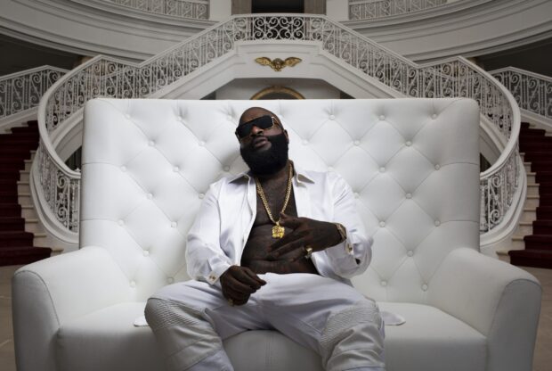Rick Ross wallpapers shows a man sitting confidently on a white sofa with gold chains and sunglasses, 2K Desktop Wallpaper