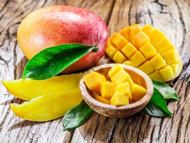 A ripe mango with sliced and cubed pieces displayed on a wooden surface, HD Desktop Wallpaper