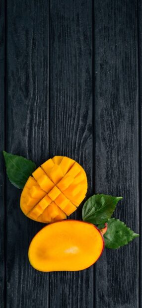 A ripe mango with one half sliced and the other half whole on a dark wooden surface, HD Phone Wallpaper
