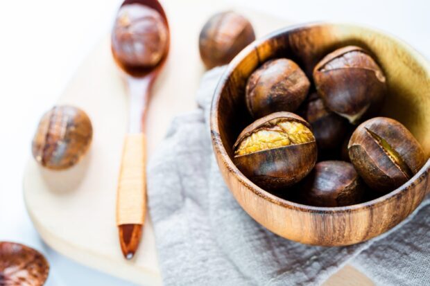 A wooden bowl filled with roasted chestnuts sits on a cloth next to a wooden spoon holding more chestnuts, HD Desktop Wallpaper