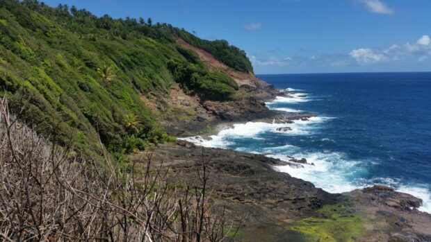 The rocky coast and green hills are shown with waves crashing on the shore in Dominica Island Wallpapers, 2K Desktop Wallpaper