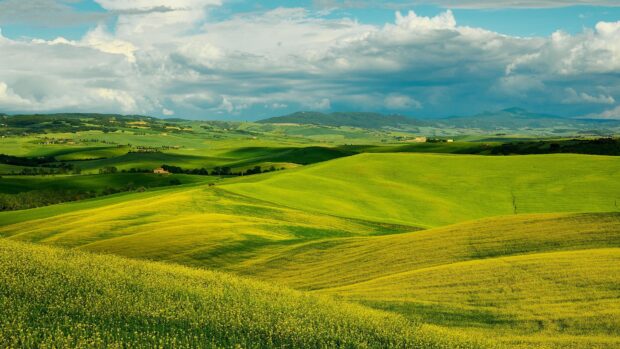 A vast landscape of green hills stretches under a partly cloudy sky with distant mountains, 4K Desktop Wallpaper
