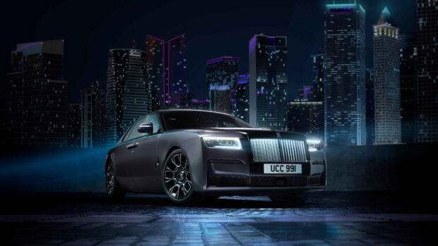 A Rolls Royce Ghost is parked in front of illuminated city skyscrapers at night, 4K Desktop Wallpaper