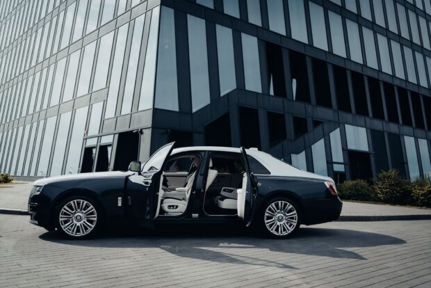 A Rolls Royce Ghost luxury sedan is parked with both doors open near a modern glass building, HD Desktop Wallpaper