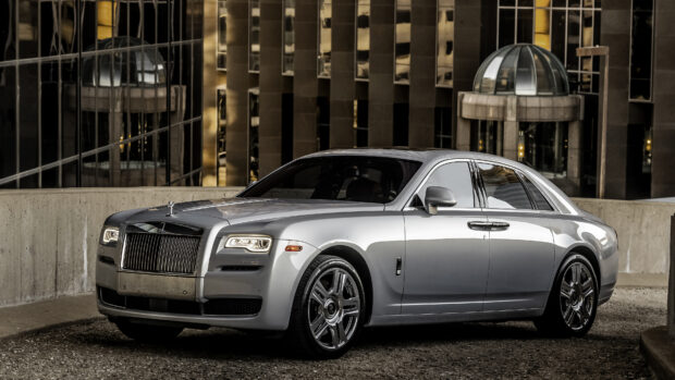 A silver Rolls Royce Ghost parked near modern buildings in a cityscape, 4K Desktop Wallpaper