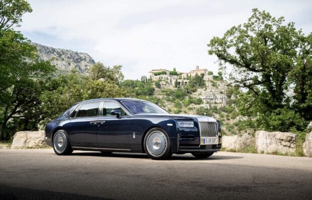 A black Rolls Royce Phantom is parked near rocky hills with greenery, HD Desktop Wallpaper