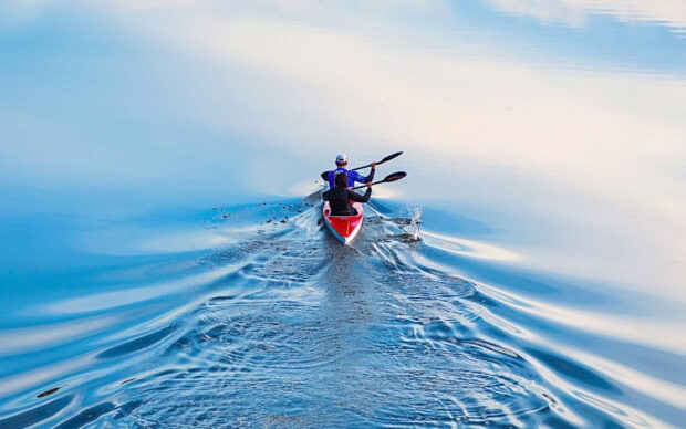 Two rowers paddling together on calm water creating ripples in the serene morning light