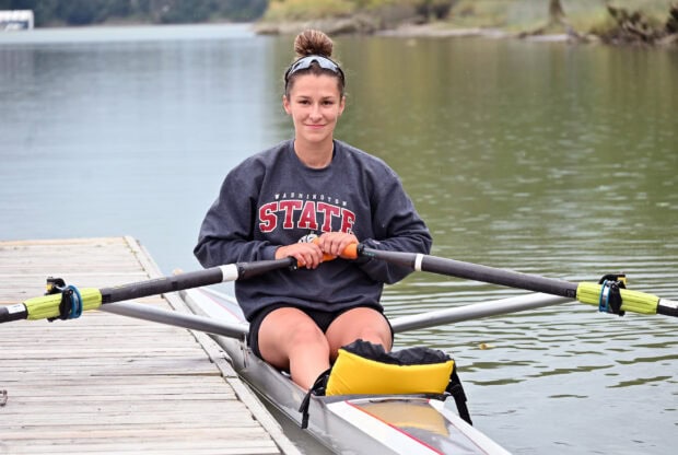 A female rowing athlete sitting in a rowing boat holding oars on a calm lake