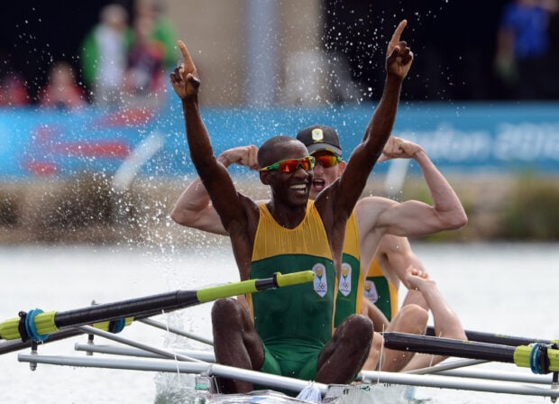 Male rowing team celebrating victory with raised arms and splashing water