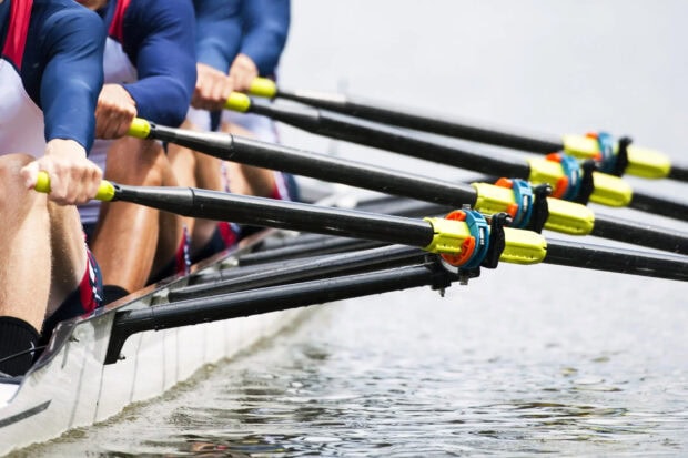 Rowers in a team rowing boat synchronizing their oars on the water surface