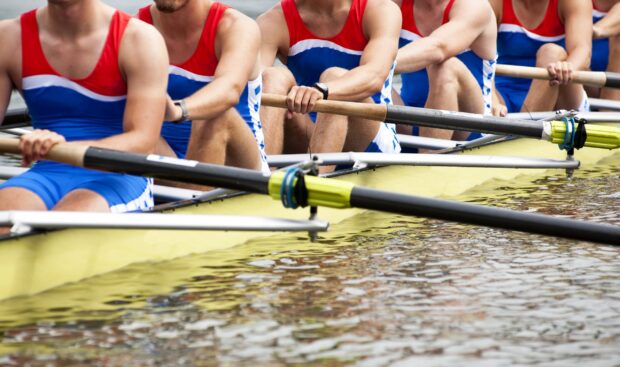 Rowers in red and blue uniforms rowing together on a yellow boat in the water