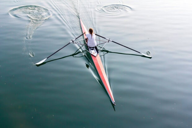 A person rowing a single scull boat on calm water during practice session