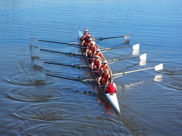 Team rowing together in a long boat on calm water during a sunny day