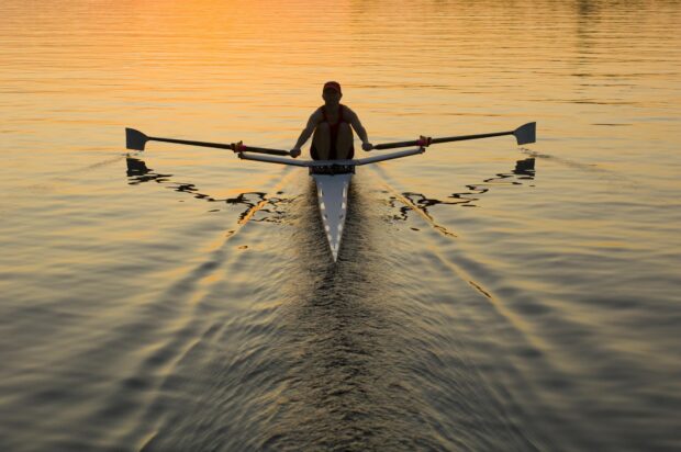 A rower paddling a single scull on calm water at sunset with smooth ripples