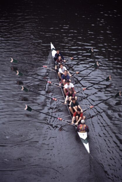 A rowing team practicing hard on the water in a long narrow boat with oars in action