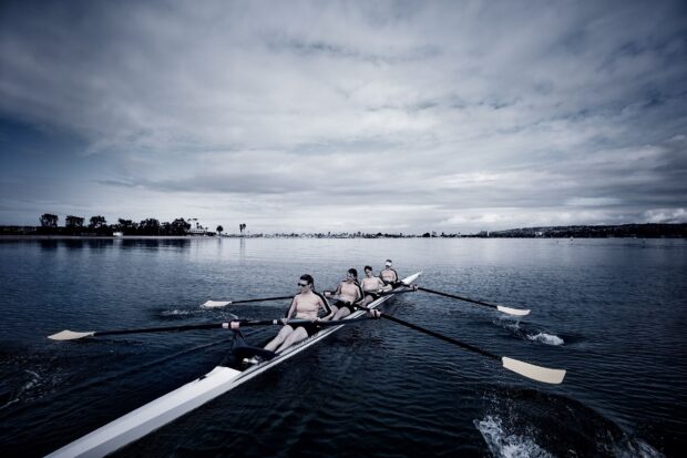 A rowing team practicing synchronized rowing on a calm lake during cloudy weather