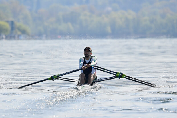 A man practicing rowing on calm water with trees in the background