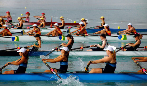 Female rowing teams compete in a rowing championship race on calm water with oars in motion