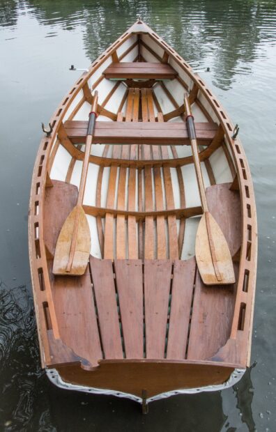 A wooden rowing boat with two oars floating calmly on the water surface