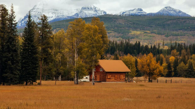 A rustic cabin stands among autumn trees with mountains in the background, HD Desktop Wallpaper