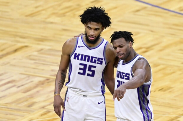 Two Sacramento Kings players in white uniforms discuss strategy on the basketball court