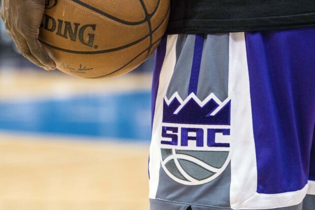 A close up of a basketball player holding the ball with Sacramento Kings shorts logo visible on the court
