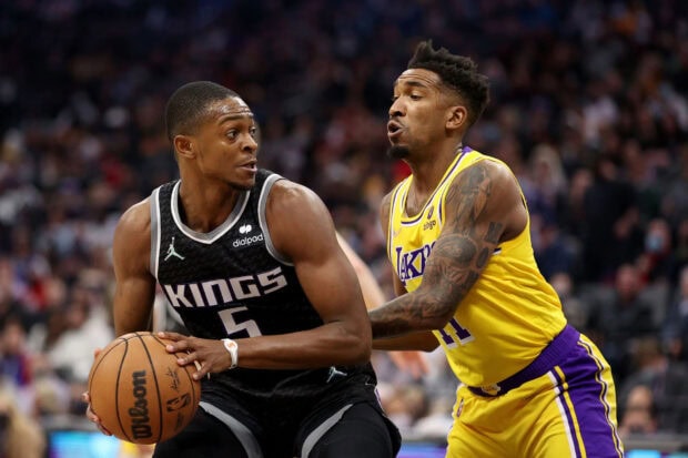 A Sacramento Kings player in a black jersey holds a basketball while guarded by a Lakers player during a game