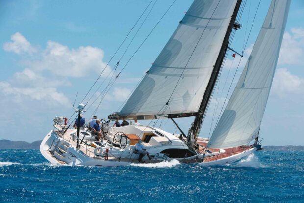 A sailing boat with crew navigating blue ocean waters under clear skies