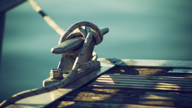 A sailing rope neatly tied around a cleat on the boat deck