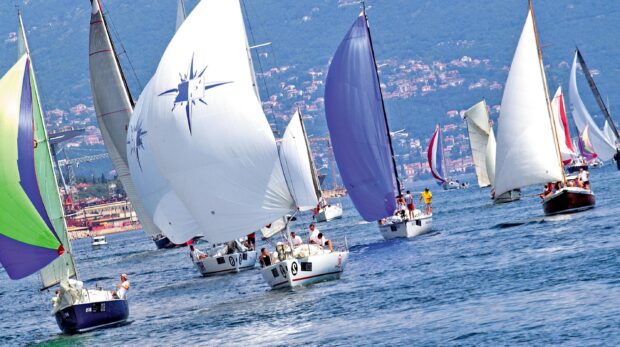 Several sailing boats racing on the calm sea near the shore with green hills in the background