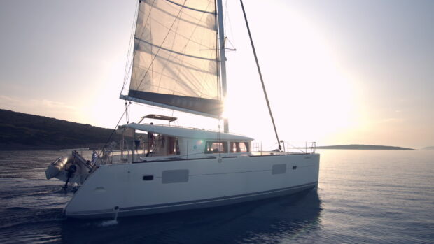 A sailing yacht gliding smoothly on calm waters near the coastline at sunset