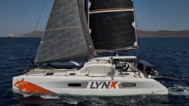 A sailing yacht with black sails glides over the blue ocean near rocky islands