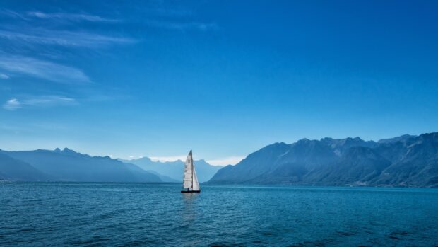 A sailing boat glides across the lake with mountain landscapes in the background