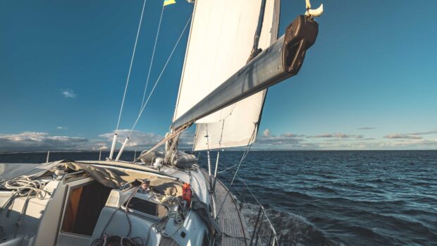 A sailing boat navigating through calm ocean waters under a clear blue sky with sails fully raised