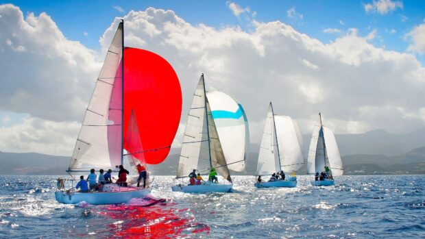 A sailing boat with a red spinnaker racing alongside other sailboats on a sunny day