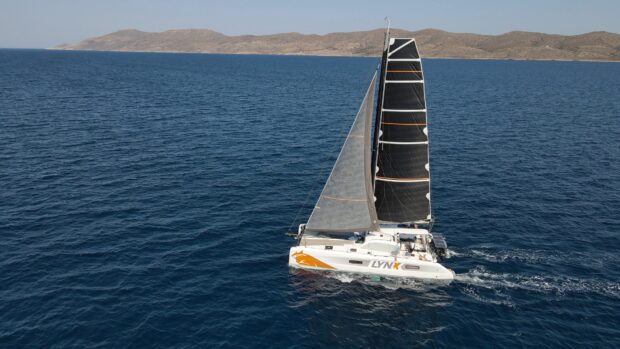 A sailing boat with black and gray sails navigating on deep blue sea near rocky coastline
