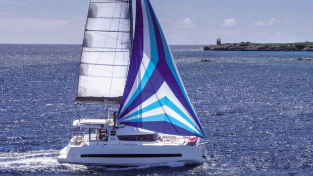 A sailing boat with colorful sails navigating the deep blue sea near the coast