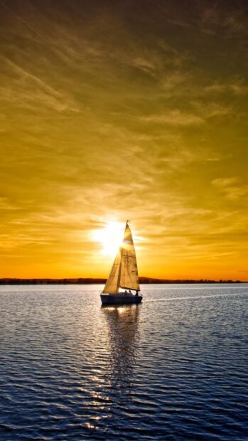 A sailing boat on calm water during sunset with a golden sky in the background