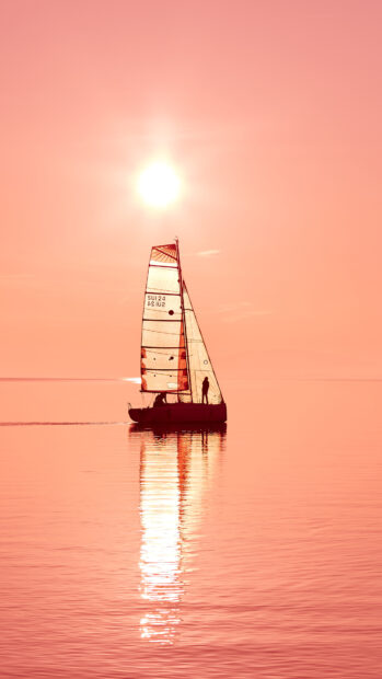 A sailboat with sails raised glides across calm water during sunset sailing