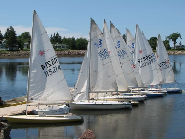 A fleet of sailing boats lined up on the calm water at the dock