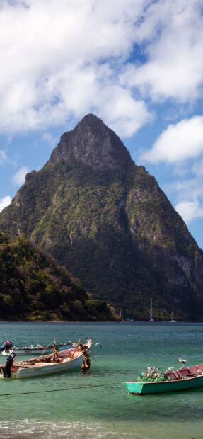 Boats floating near a mountain in Saint Lucia with clear water and birds flying