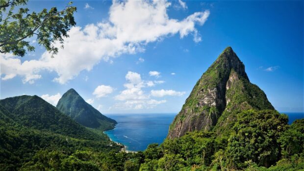 The lush green mountains of Saint Lucia meet the blue sea under a bright sky with clouds