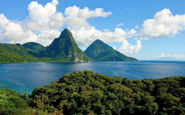 Two green mountains rise above the blue sea in Saint Lucia landscape with a cloudy sky