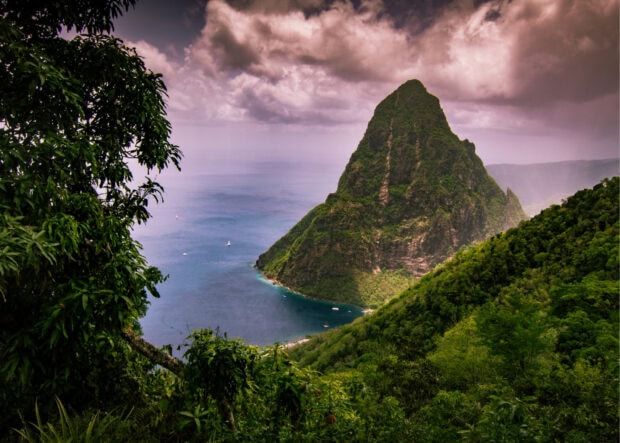 Lush green hills surround the famous Saint Lucia mountain peak under a cloudy sky