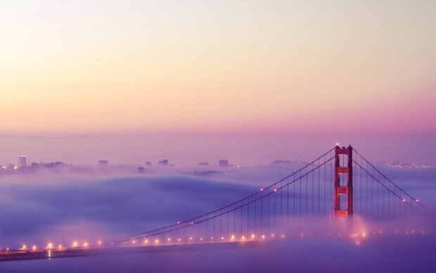 San Francisco skyline with fog rolling over the city and the iconic bridge illuminated at dusk
