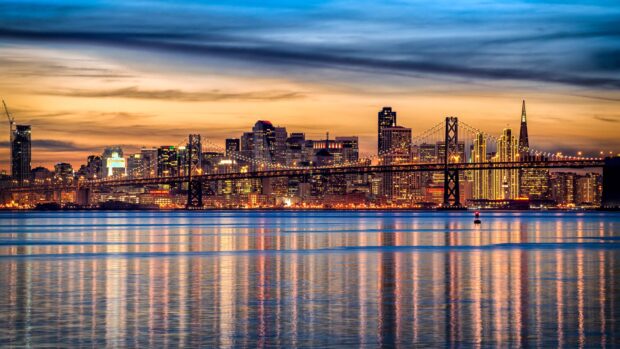San Francisco skyline with illuminated buildings and bridge reflecting on water at sunset