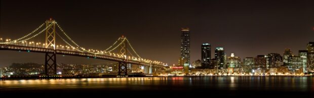 San Francisco skyline with illuminated bridge and city lights reflecting on water at night