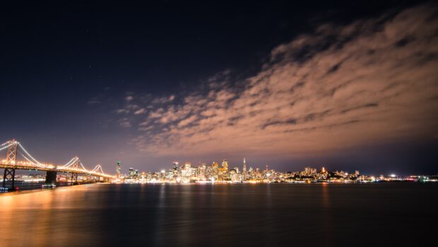 The San Francisco skyline at night with illuminated buildings and a lit up bridge under a starry sky
