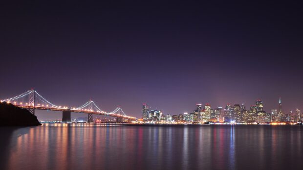 San Francisco skyline view with illuminated bridge and city lights reflecting on water at night