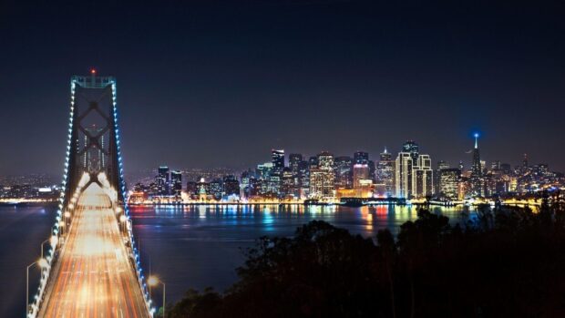 San Francisco skyline at night with illuminated buildings and the lit bridge in the foreground